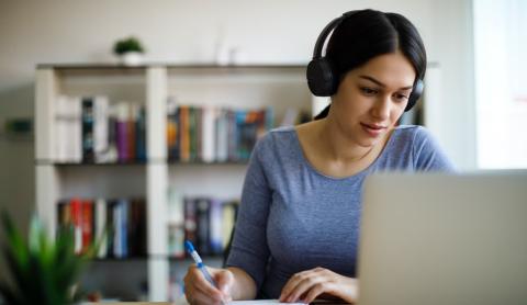 Young woman taking notes while watching her laptop
